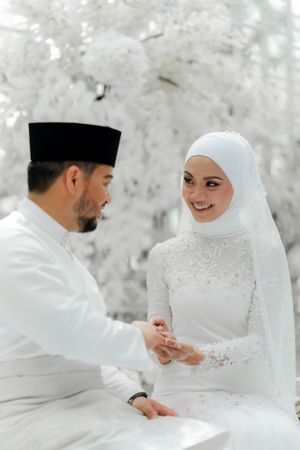 Traditional Muslim wedding ceremony with couple in white attire exchanging rings.