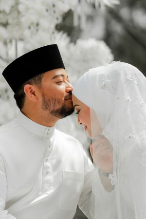 Intimate moment between newlyweds in traditional white Muslim wedding attire.
