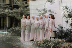 Bridesmaids in soft pink modest dresses pose together in garden setting.