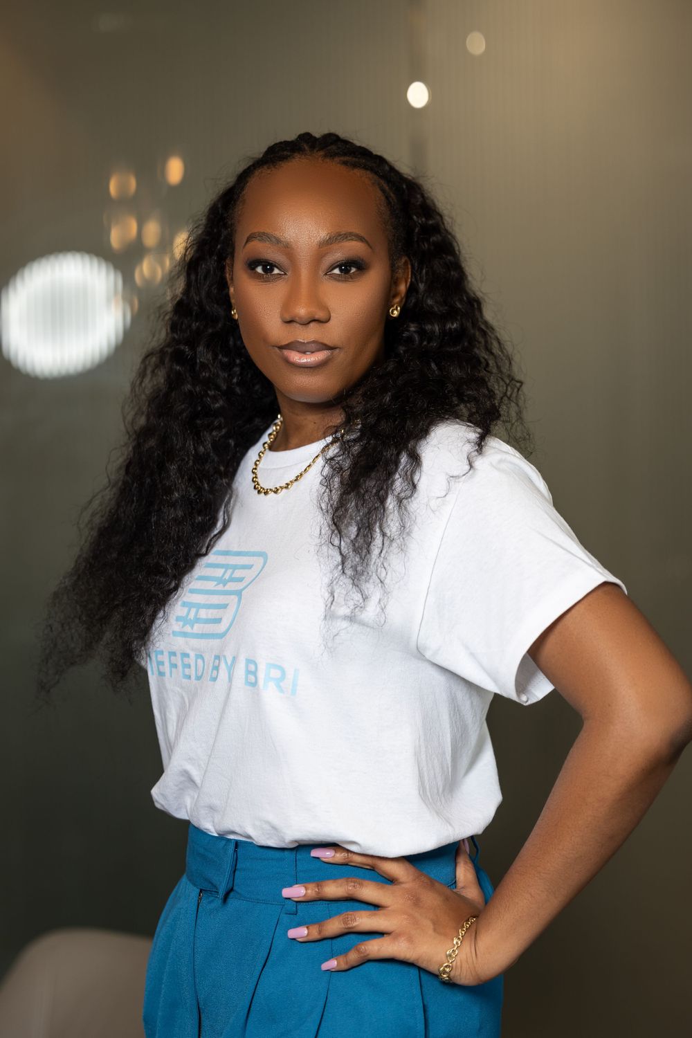 Stylish professional in white t-shirt and blue pants with long curly hair posing confidently.