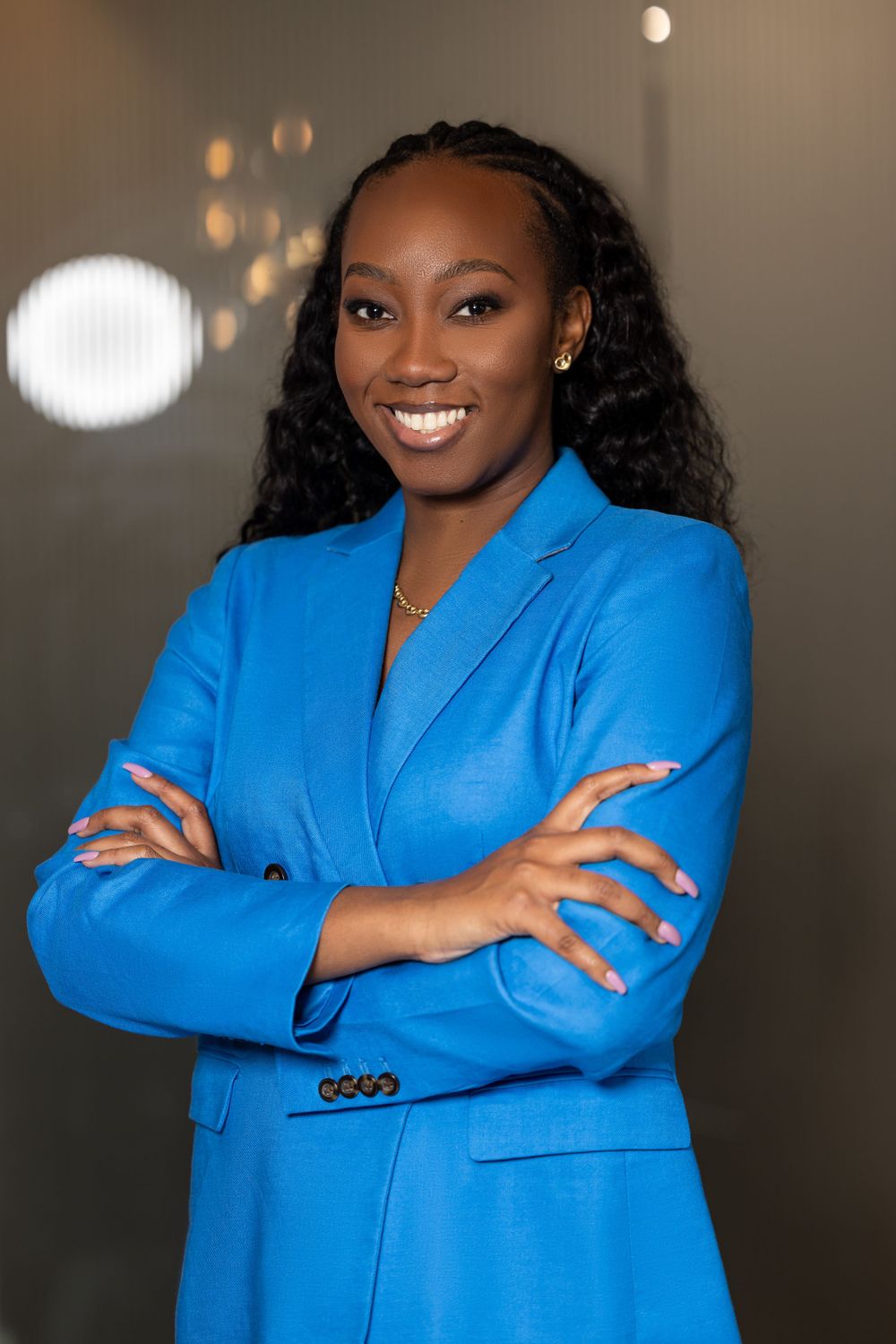 Confident professional in electric blue blazer with arms crossed against stylish bokeh background.