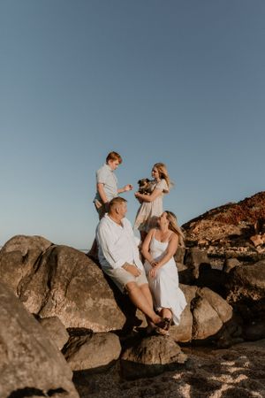Family gathered on coastal rocks at sunset in casual white outfits creating an intimate outdoor portrait, in Karratha, WA