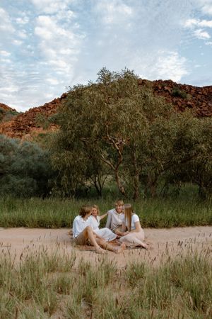 Three siblings celebrate their mum as they talk and laugh on a picnic rug, set against the rocky hills and golden grasses of Karratha, WA