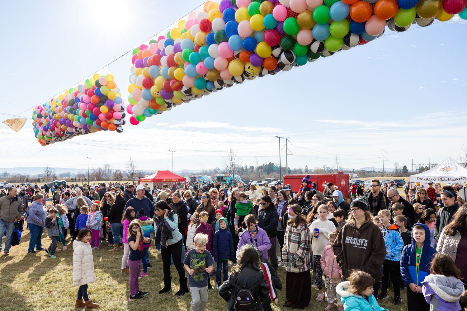 Large crowd gathered under colorful balloon arch at outdoor festival or fair.