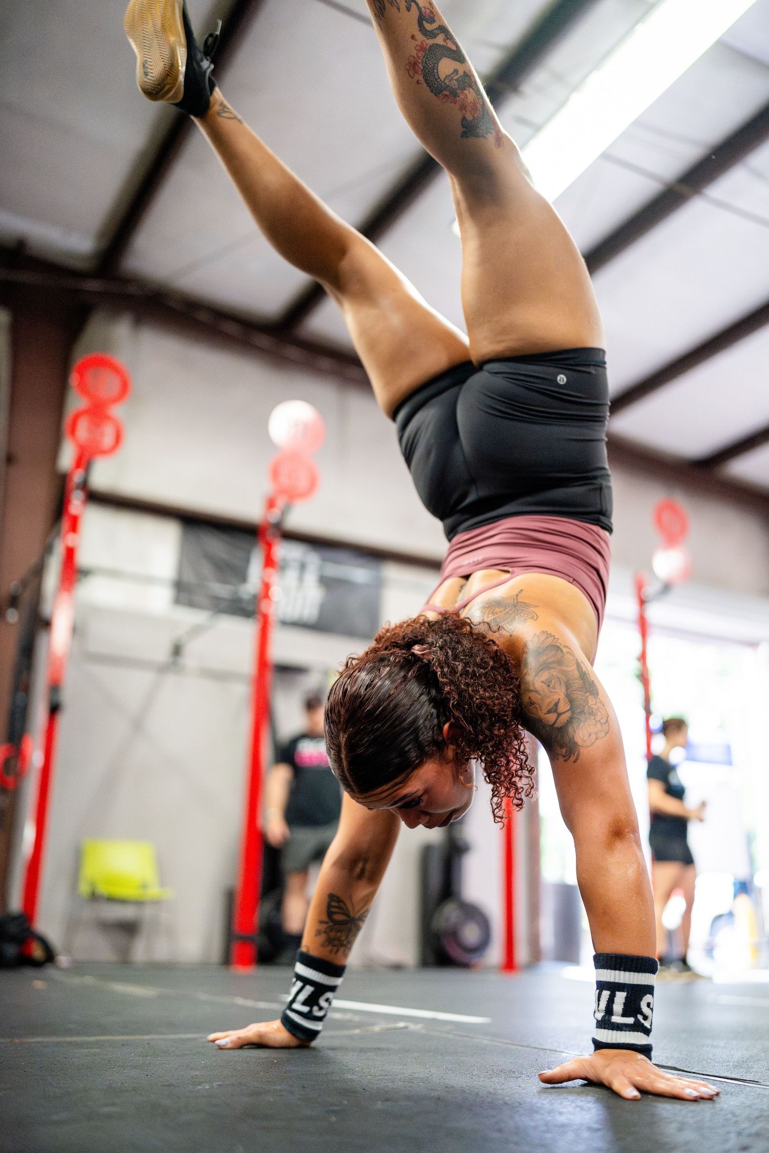 CrossFit athlete performs handstand push-up against gym wall with red lights.