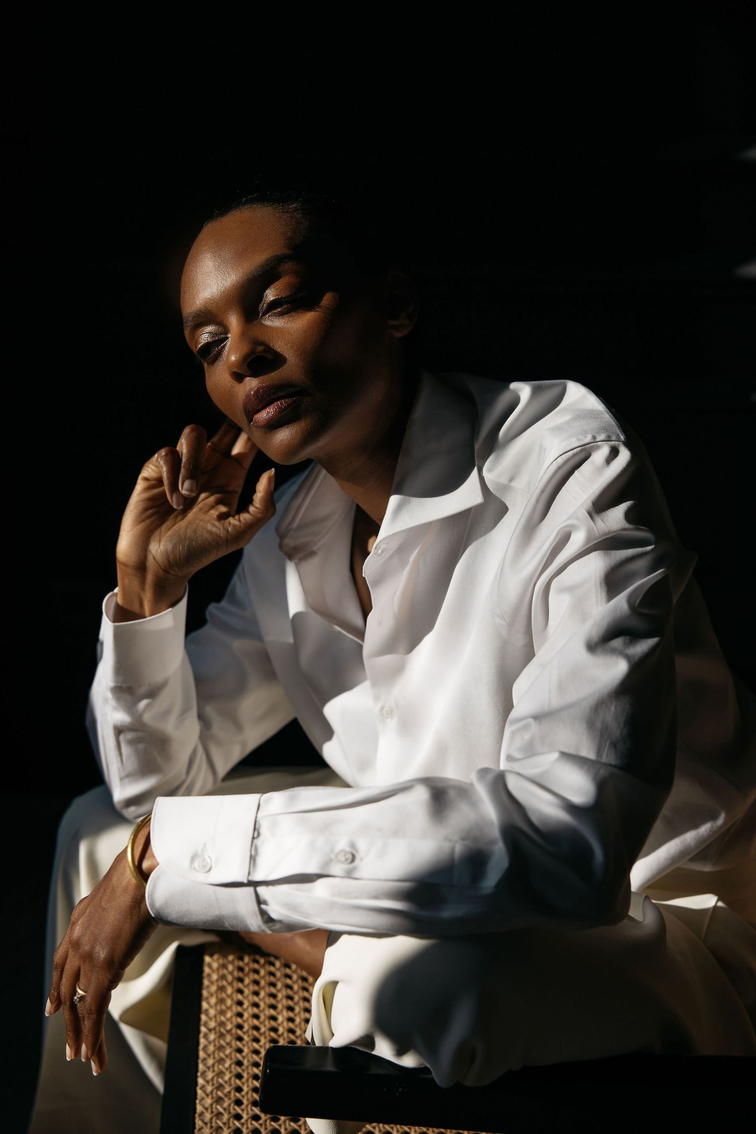 Dramatic portrait of someone in a crisp white shirt against a dark background.
