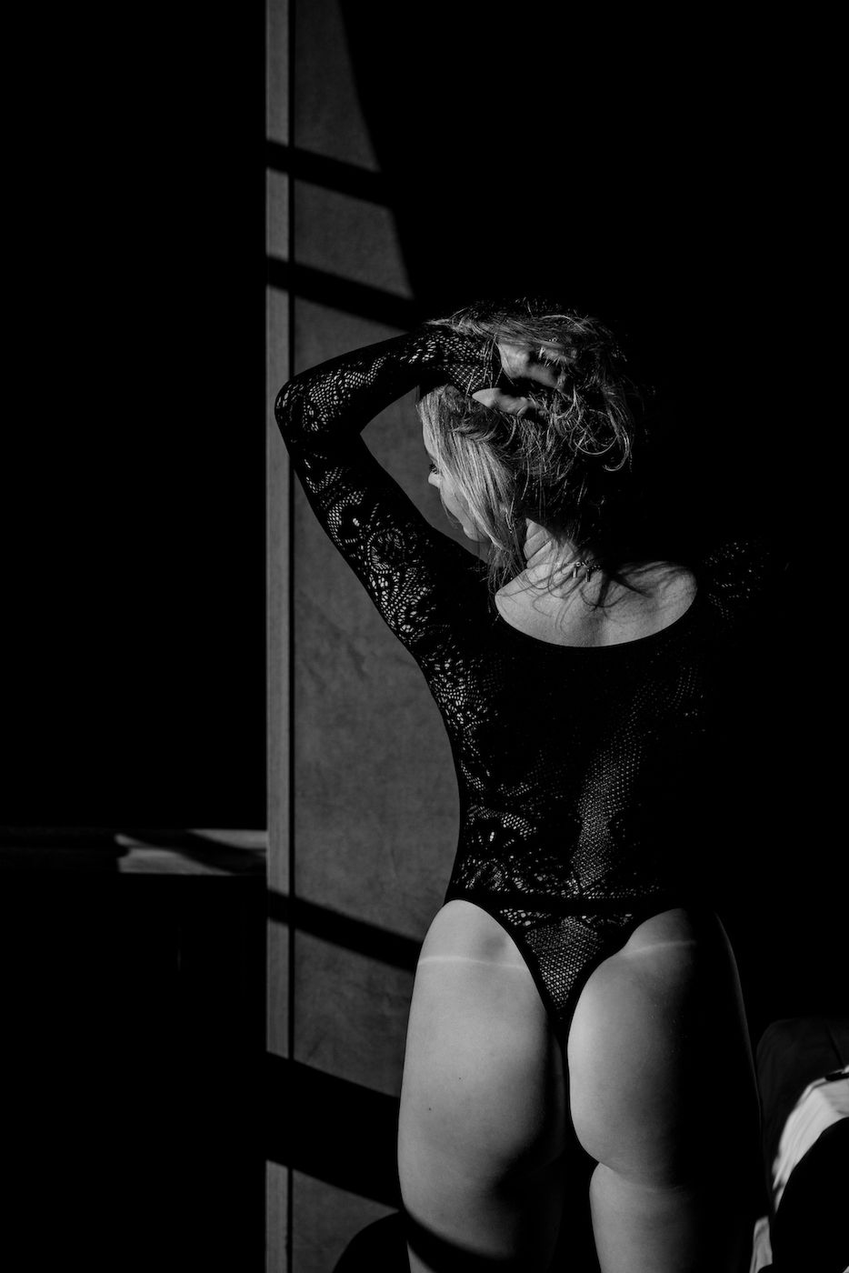 Artistic black and white boudoir photo with dramatic window lighting and shadows.