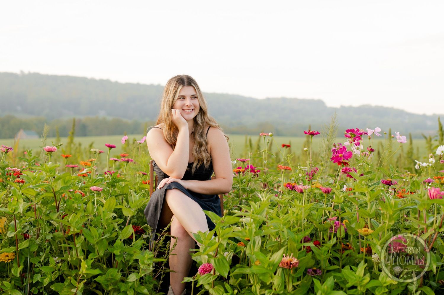 Outdoor summer portrait session among blooming pink cosmos flowers with hills in the background.
