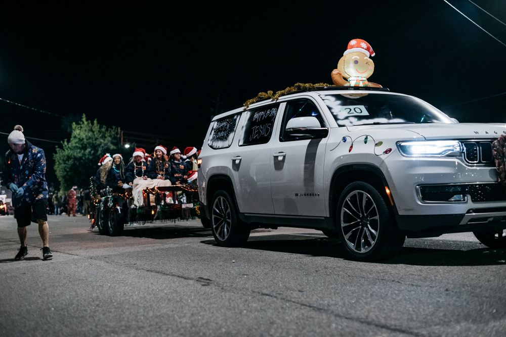 SUV with figure on roof during nighttime parade or event.