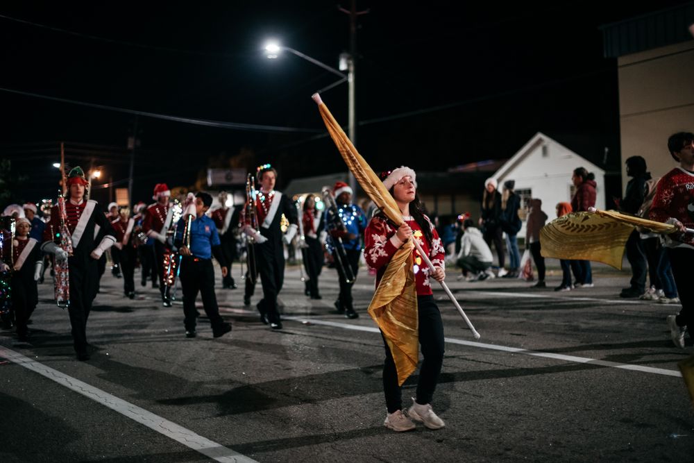 Marching band performer twirls baton during nighttime parade performance.