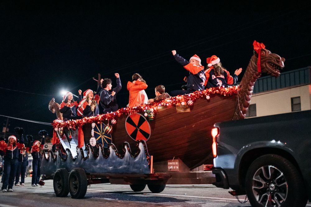 Holiday parade procession with decorated vehicles and lights moving through a dark street.