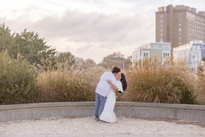 Man dips woman in a romantic pose surrounded by autumn grasses with city skyline in background in Asbury Park, NJ.