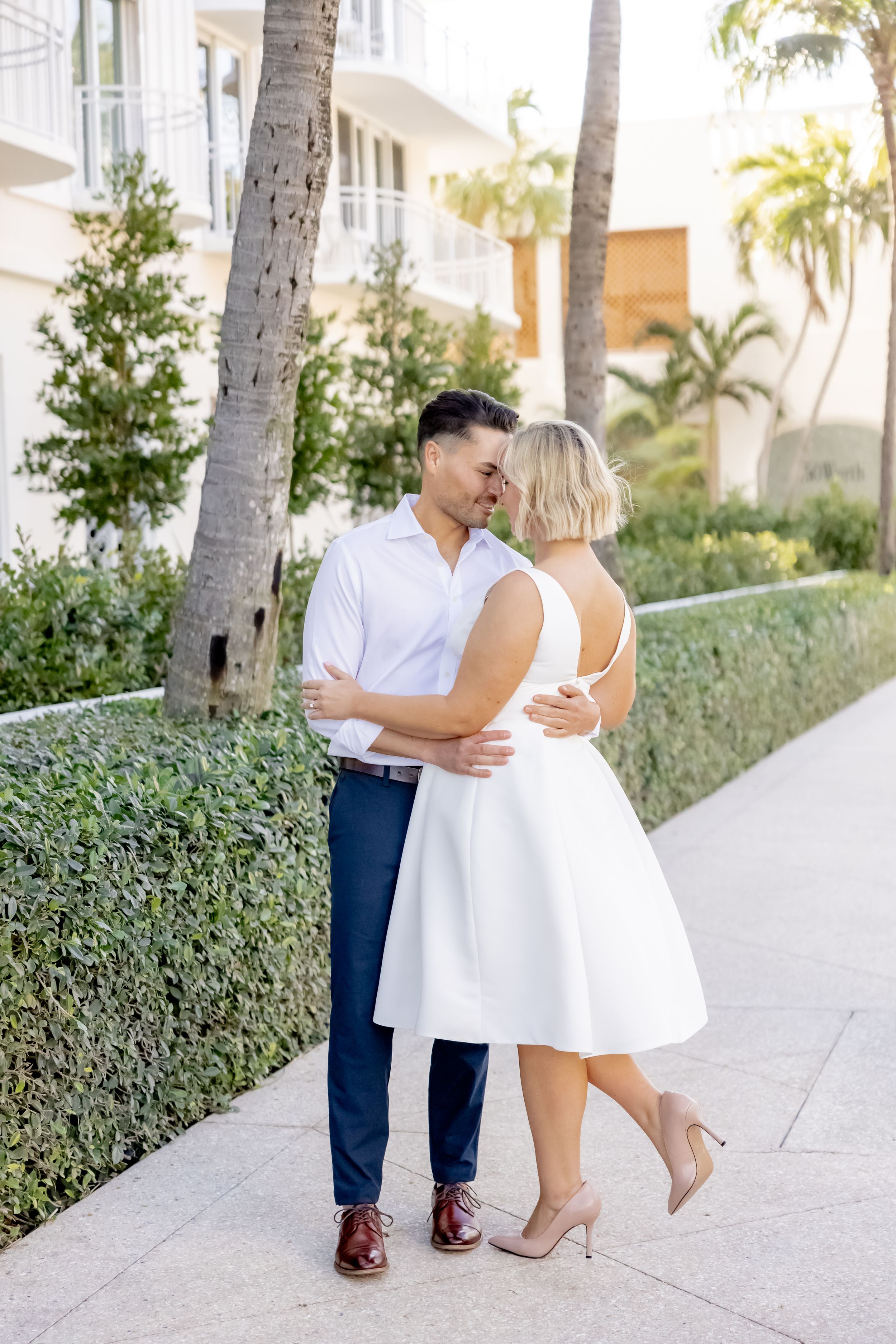 Couple share a romantic kiss on a palm tree-lined walkway  in Palm Beach, Florida.