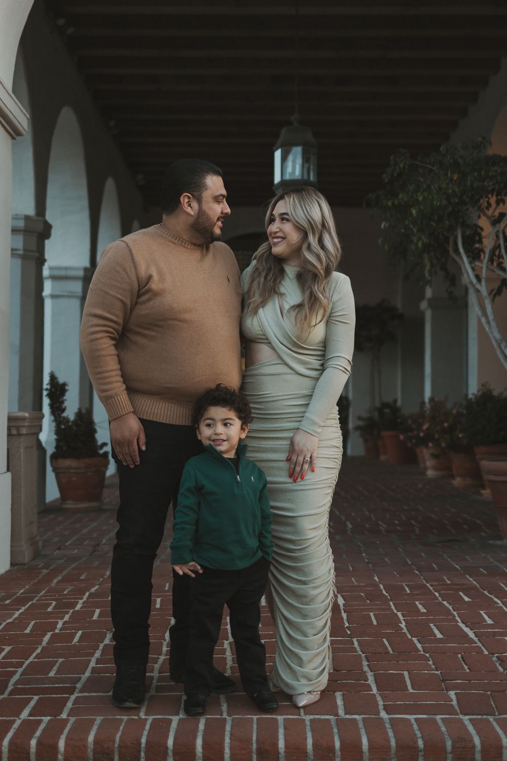 A family poses together in formal attire against an architectural backdrop with arches and terracotta flooring.