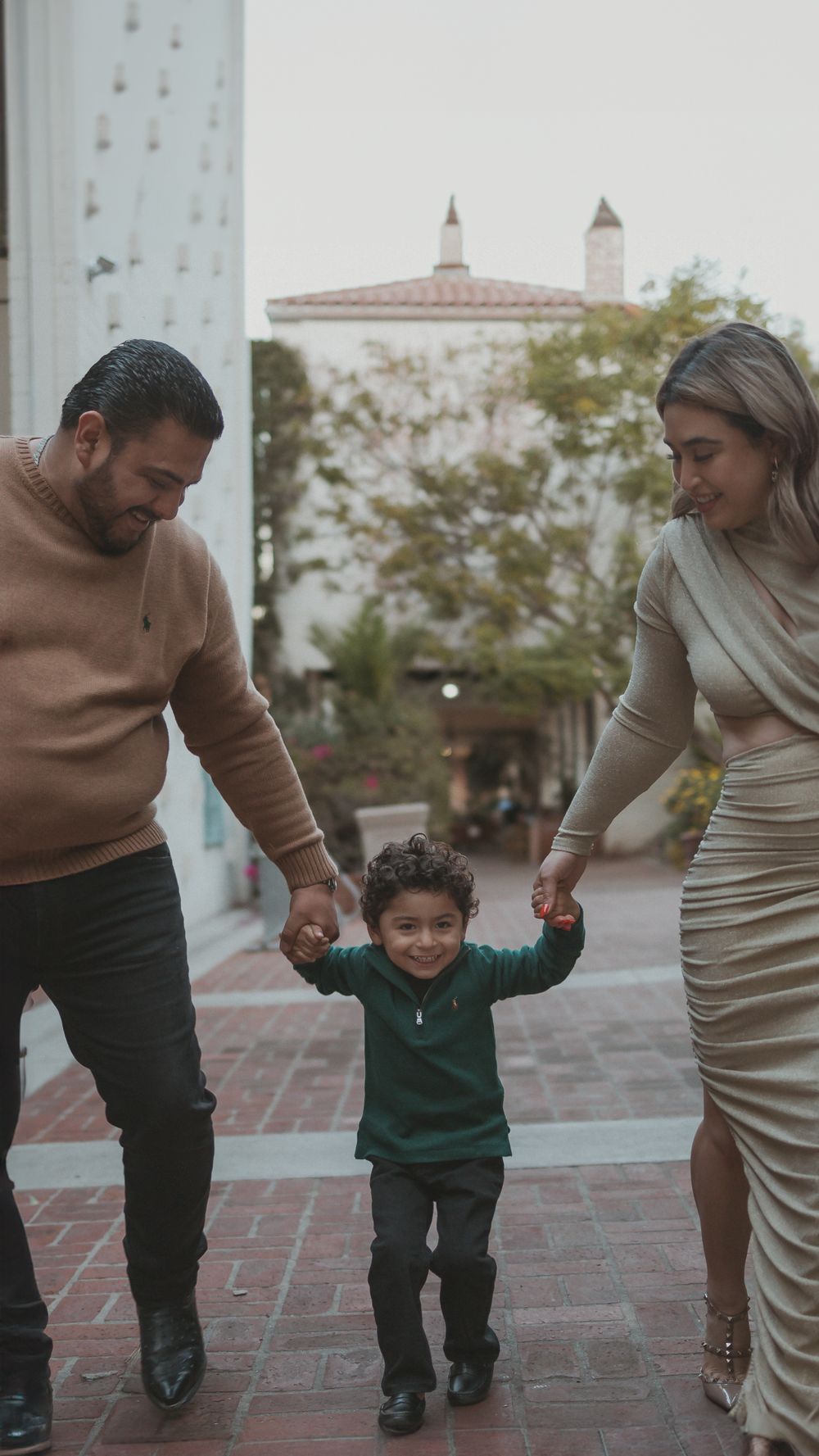 A family walking together on brick pavement with Spanish-style architecture visible in the background.