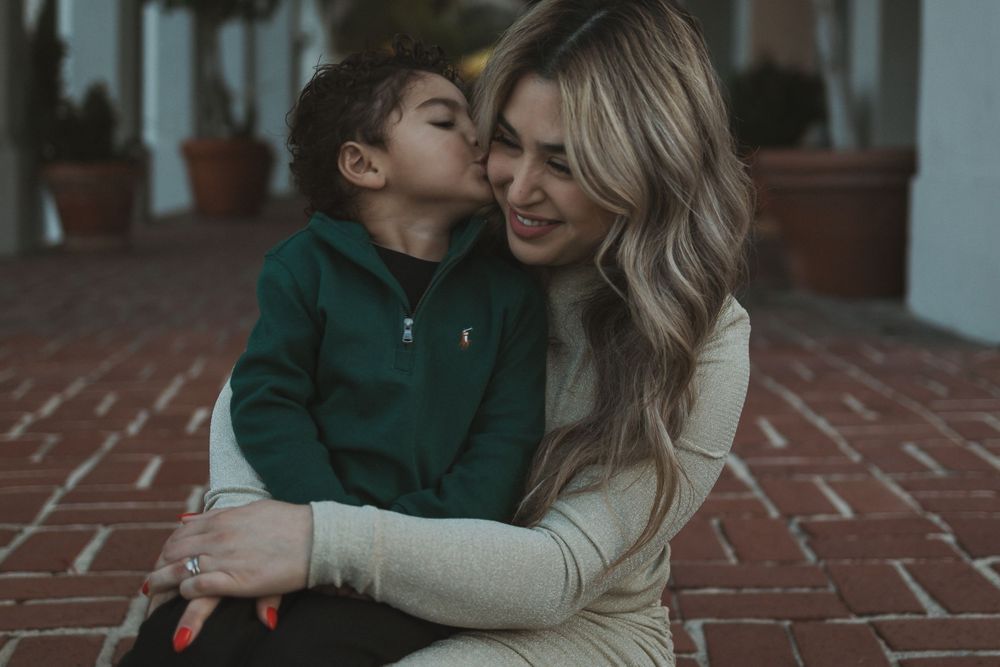 A tender moment captured between parent and child wearing coordinated neutral tones on a brick terrace.