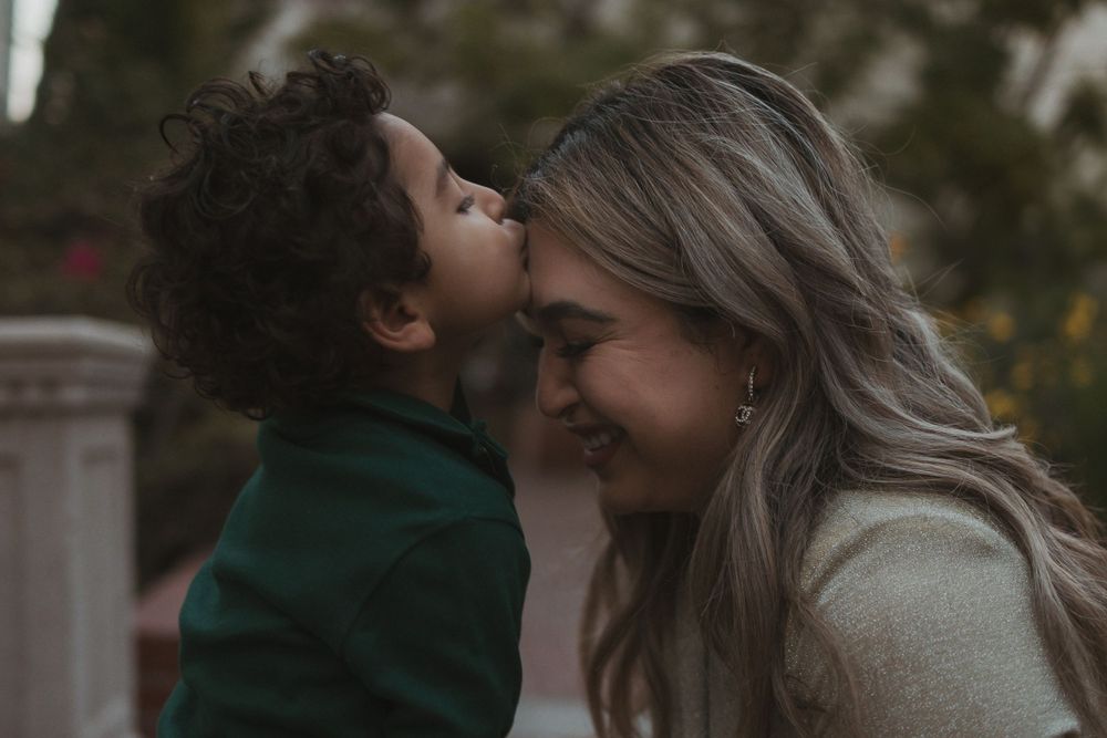 Candid outdoor portrait capturing intimate family affection in warm lighting.