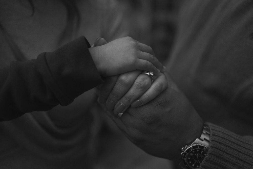 Close-up black and white photo of hands touching with wedding ring detail.