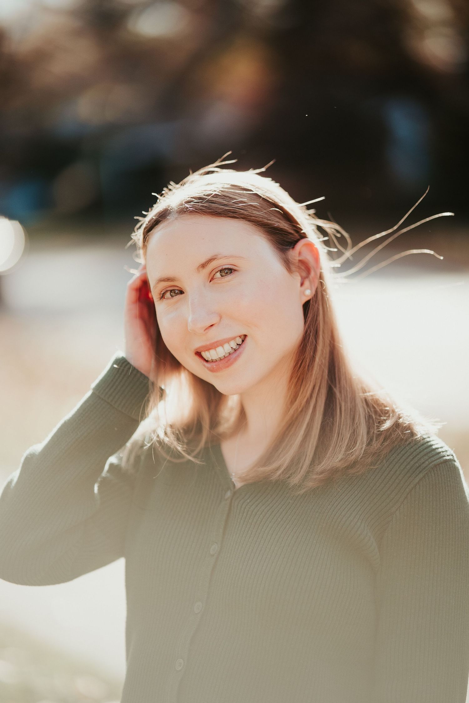 Sun-lit portrait with a genuine smile and windswept hair wearing a green sweater in soft natural lighting.