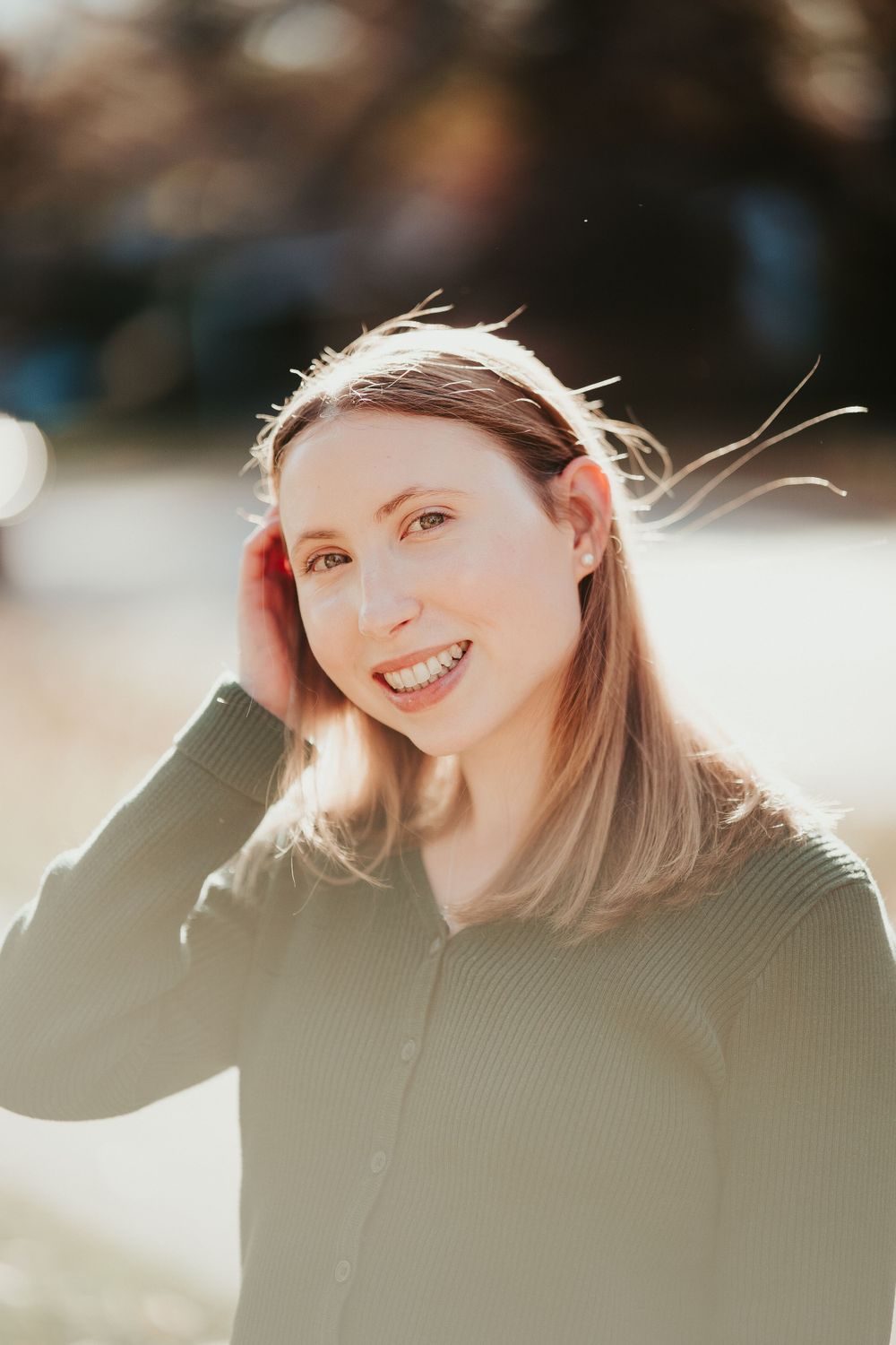 Sun-lit portrait with a genuine smile and windswept hair wearing a green sweater in soft natural lighting.