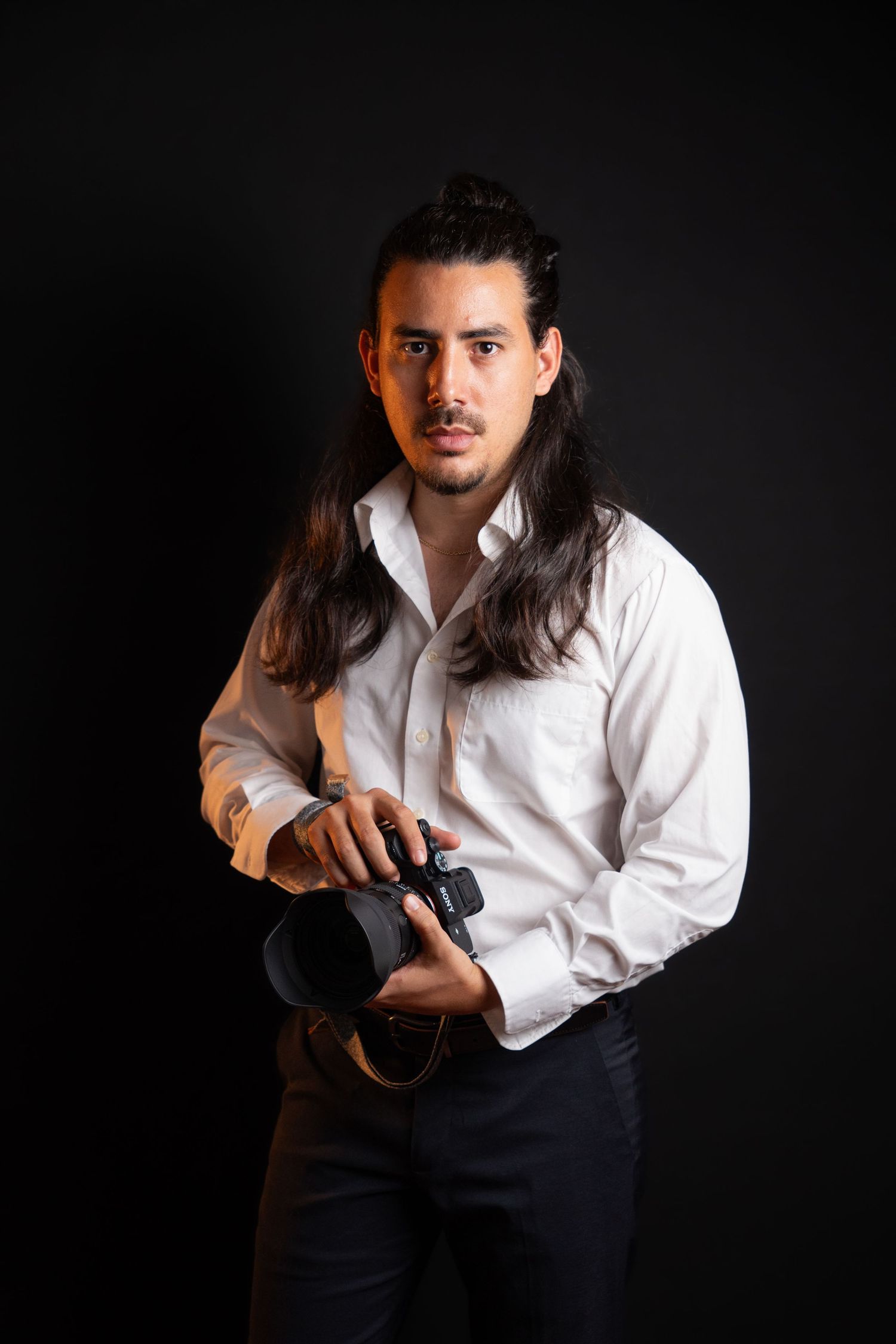 Portrait of Miami photographer Manuel Okata holding a professional camera in the studio, founder of OkataStudio.