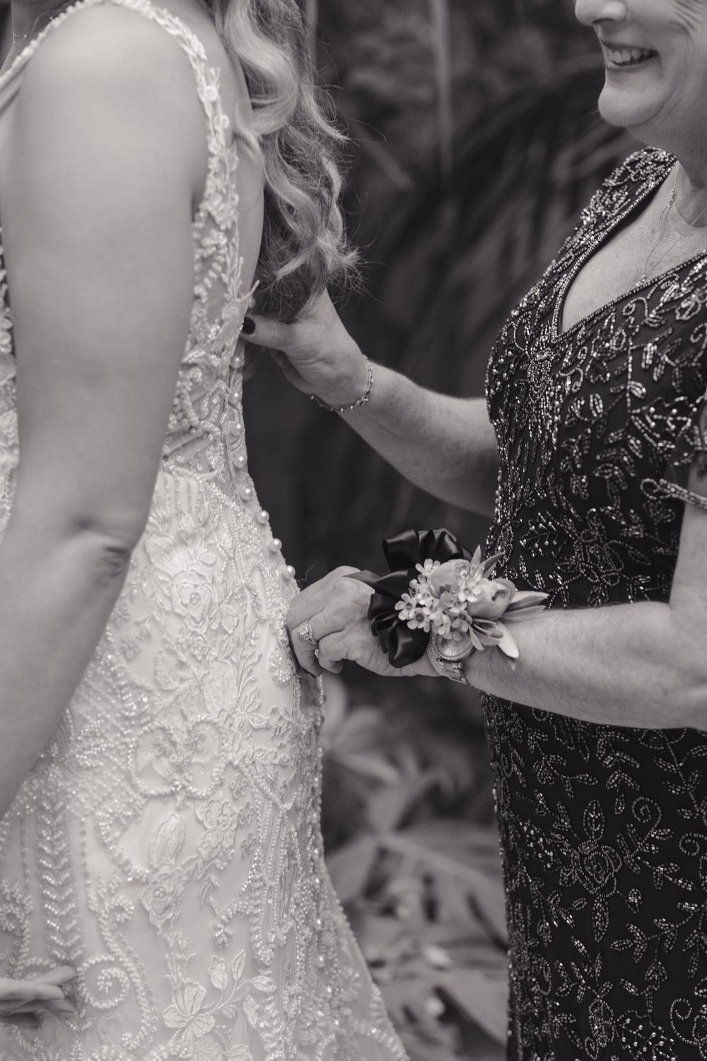 Black and white photo showing details of an ornate lace wedding dress and formal attire during a wedding moment.