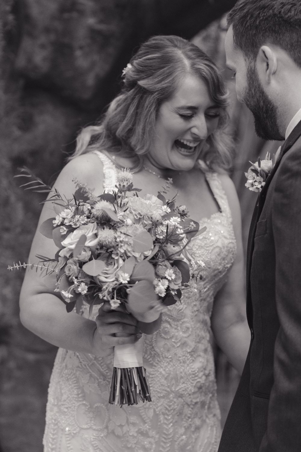 A joyful bride laughing while holding a stunning floral bouquet during her wedding ceremony.
