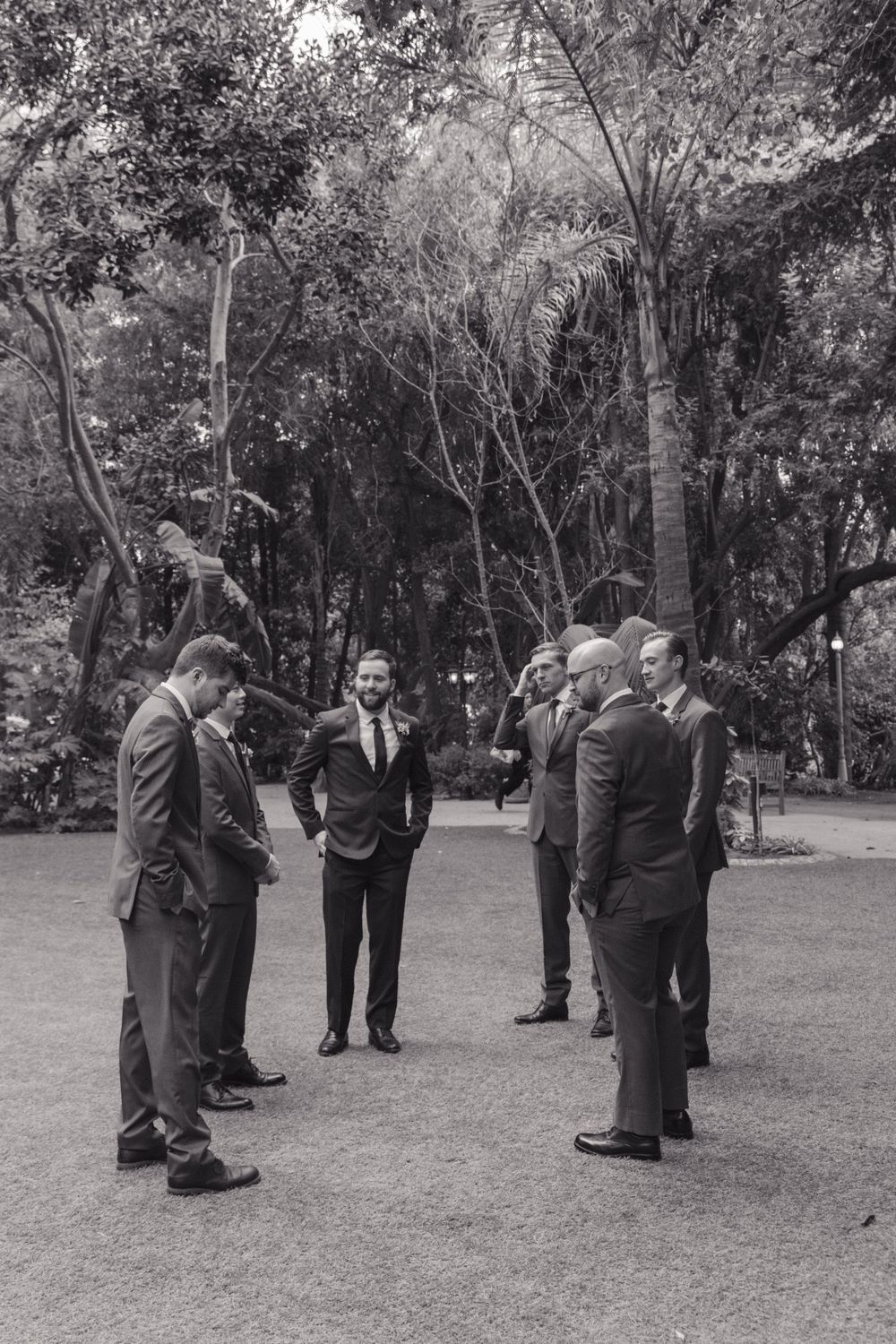 A group of formally dressed people gather in a garden setting in black and white photography.