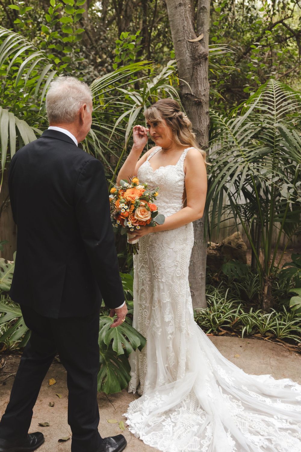 A wedding ceremony moment in a lush garden setting with tropical plants and a flowing white bridal gown.