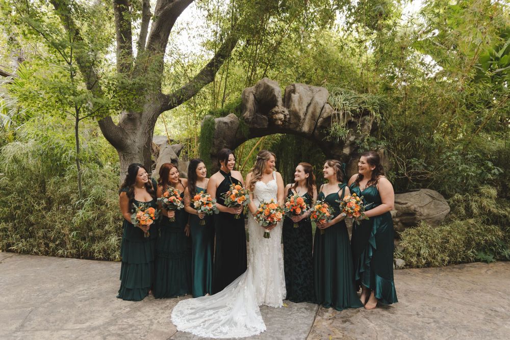 A bridal party wearing elegant emerald green dresses poses together in a garden setting.