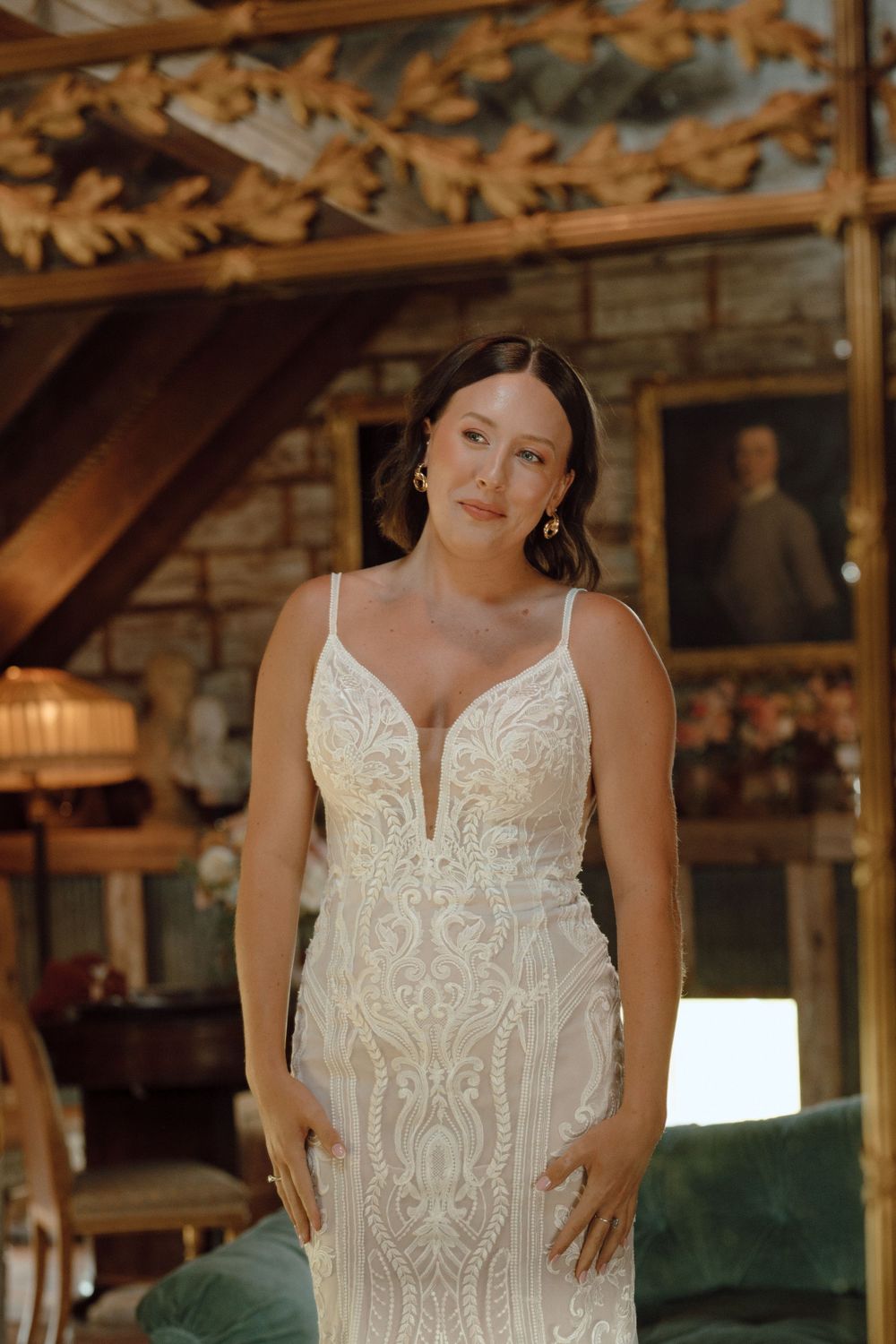 Elegant figure in an intricately detailed white lace wedding dress stands in rustic wooden barn venue.