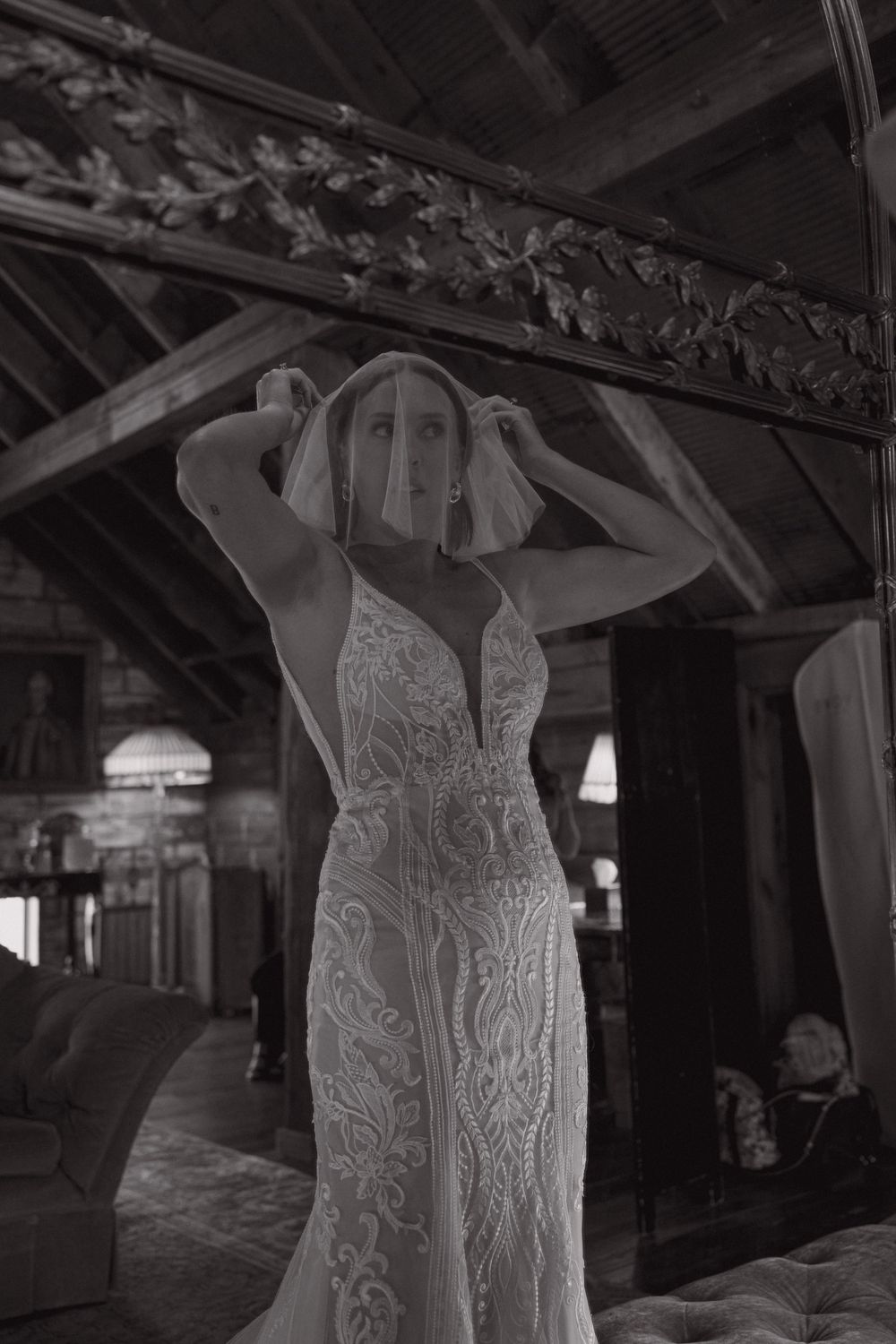 A close-up black and white photo of an intricate lace wedding dress with spaghetti straps and detailed embroidery.