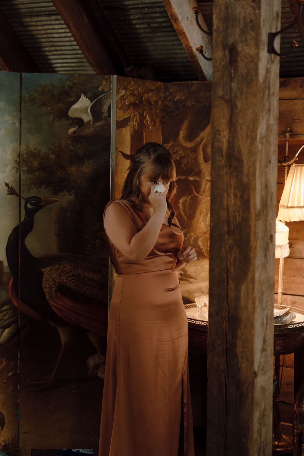 Person in a copper-colored dress poses in a rustic, dimly lit interior setting.