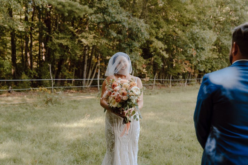 A bride in a white dress holds a floral bouquet while facing away from the camera in an outdoor setting.