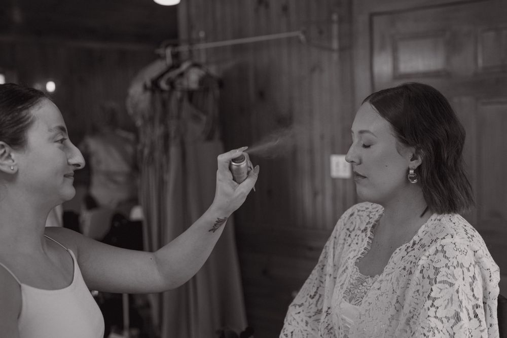 Two friends getting ready at a makeup session with one applying makeup to the other in black and white photography.