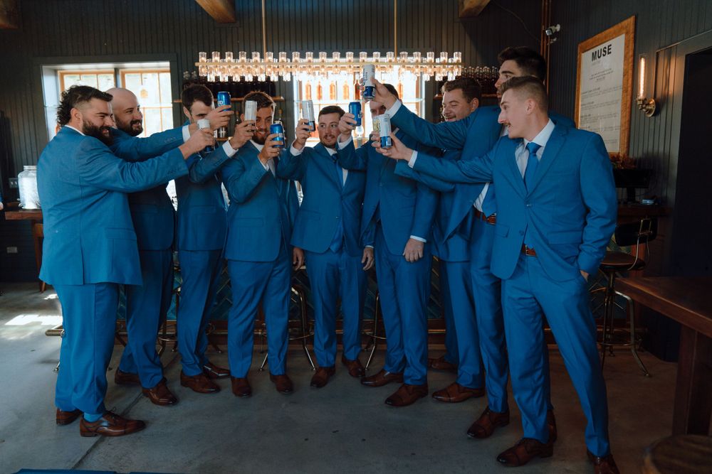 Groomsmen in matching bright blue suits toast together in celebration.