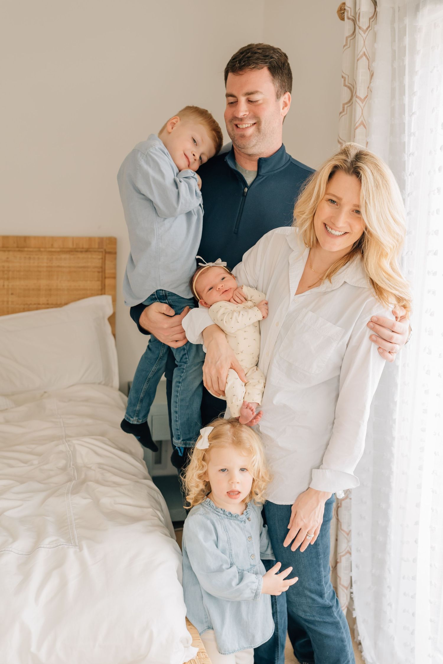 Parents cuddling newborn and two siblings in master bedroom during lifestyle photography session in Spring Lake NJ home.