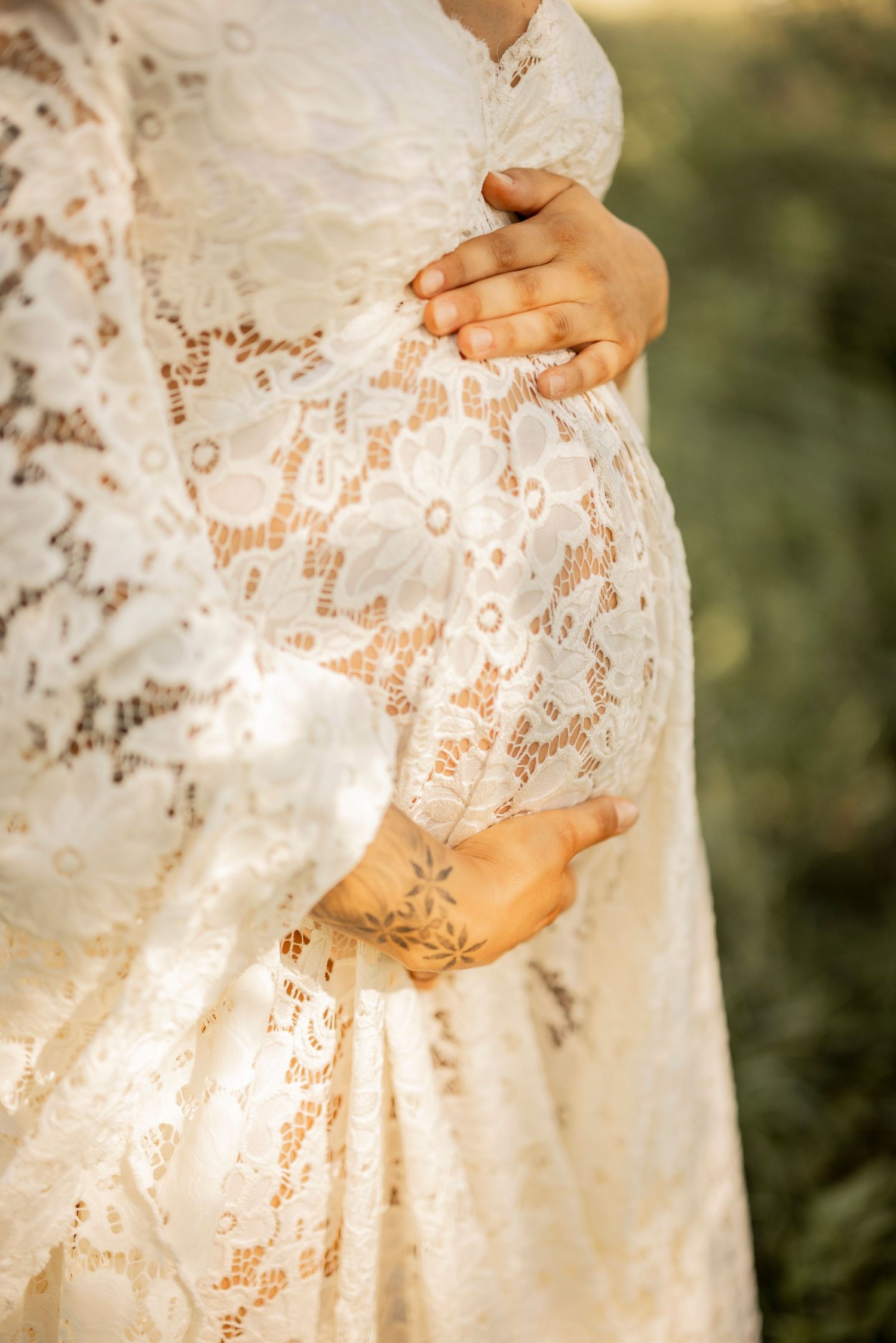 Close up of hands wearing wedding rings resting on delicate white lace wedding dress fabric.