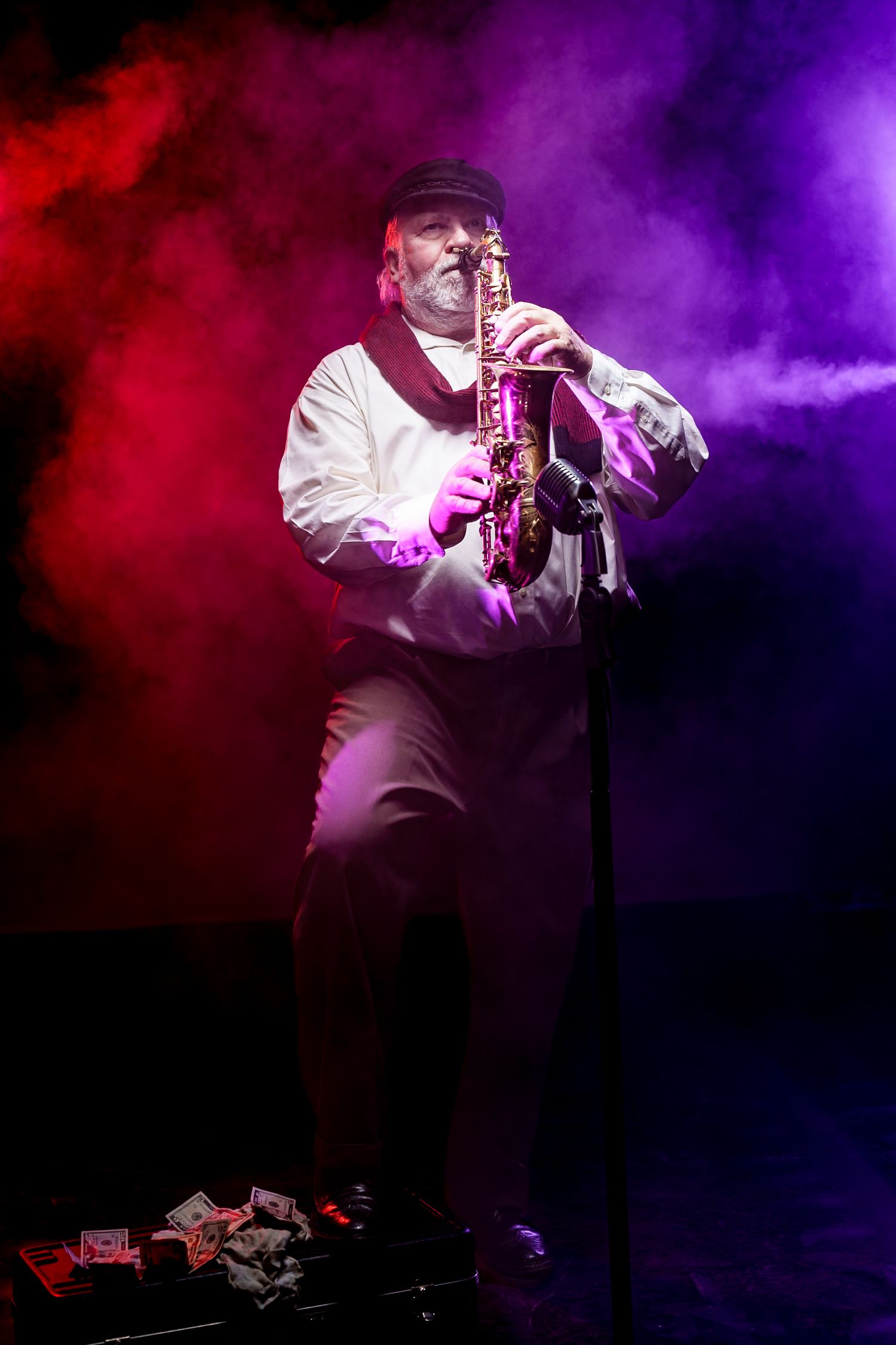 Musician plays saxophone on stage with dramatic red and purple smoke effects in theatrical lighting.
