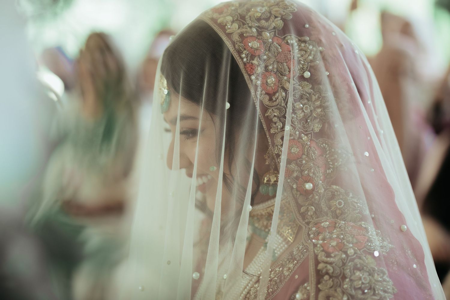 Two people in white attire exchange garlands during a wedding ceremony under a floral arch decoration.