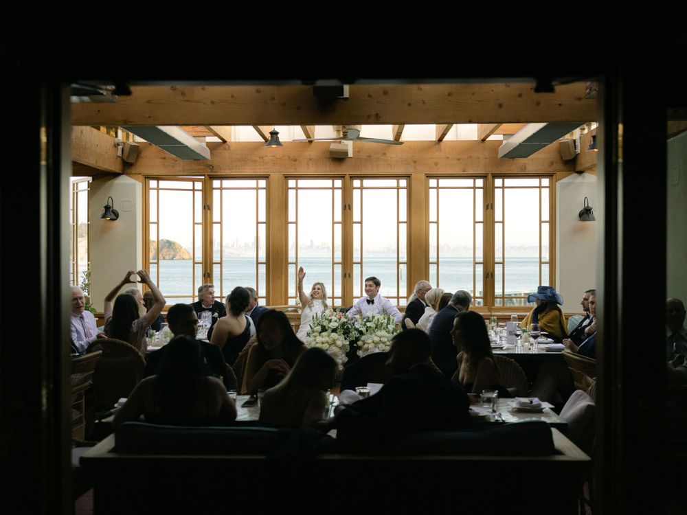 Diners seated in a dimly lit restaurant with large windows and elegant floral centerpieces on the tables.