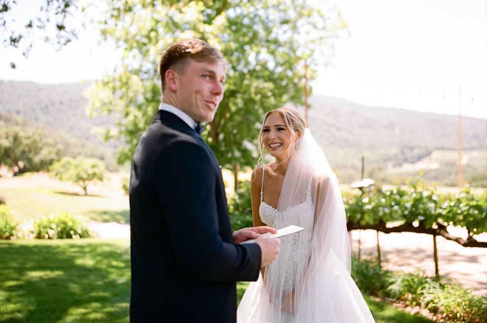 A happy couple exchanges vows during an outdoor wedding ceremony on a scenic hillside surrounded by greenery.