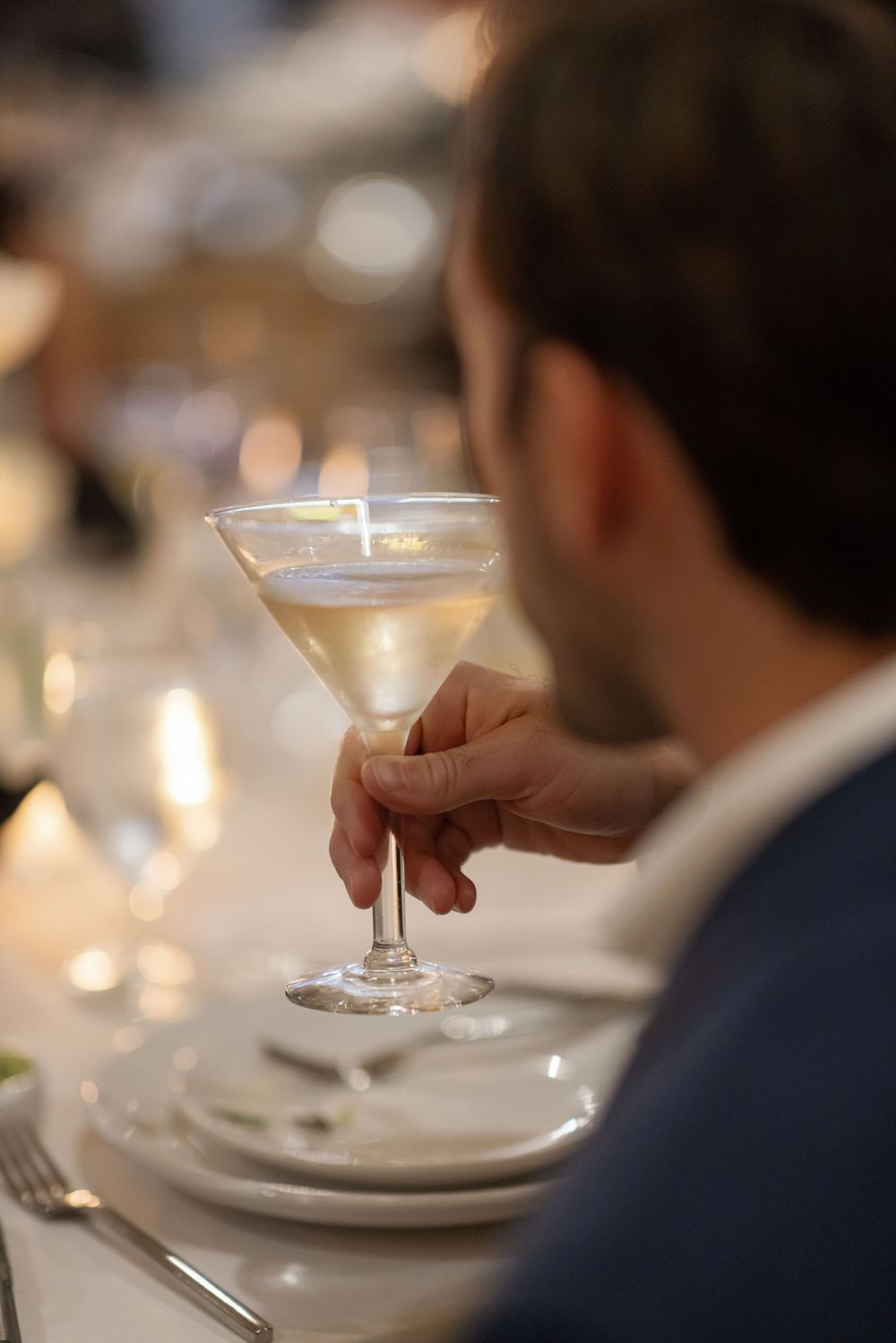 A person holds an elegant cocktail glass filled with a creamy martini at an upscale dining table with soft bokeh lighting.
