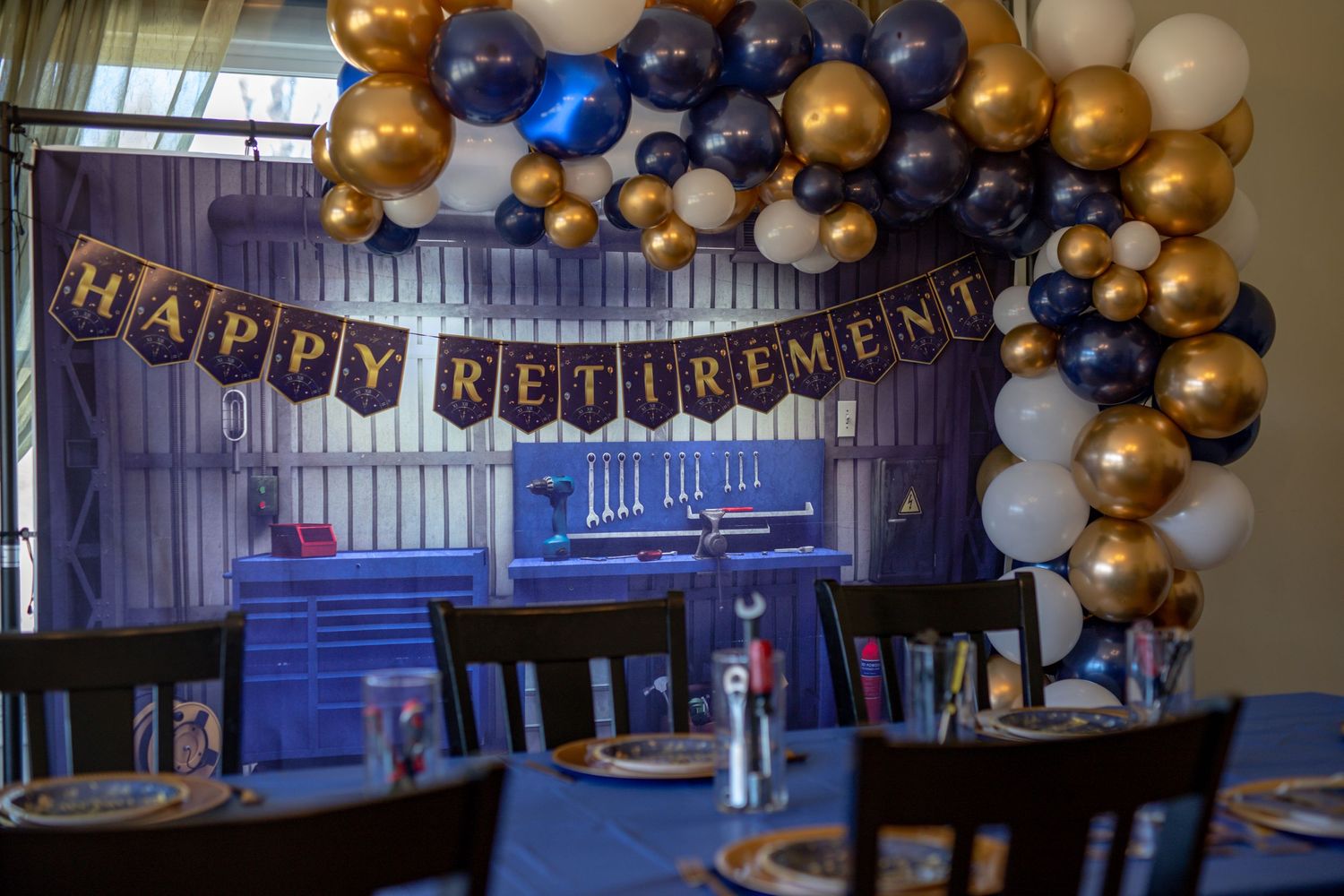 Navy and gold balloon arch with 'Happy Retirement' banner decorating an indoor celebration space.