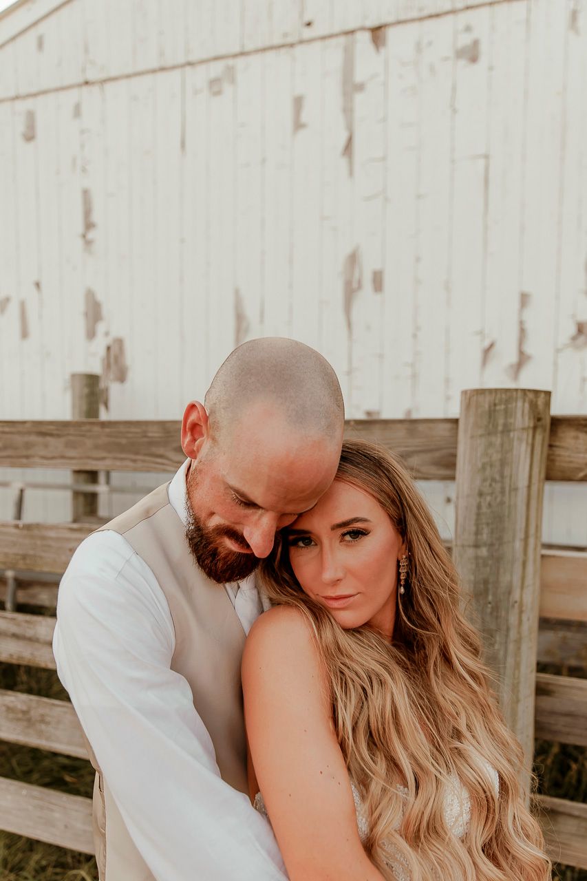 Romantic couple sharing an intimate moment against a rustic white barn wall at sunset.
