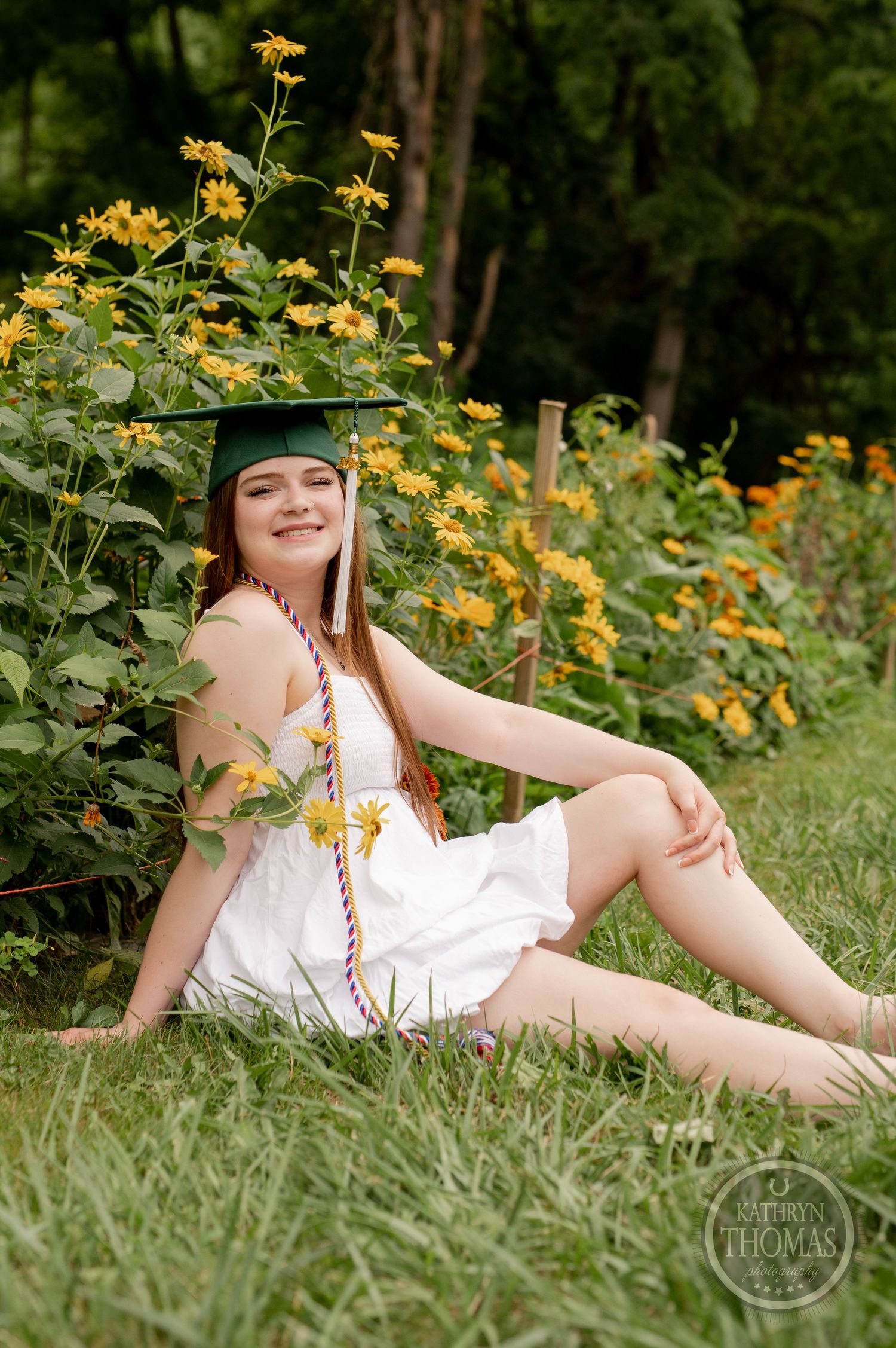 Graduate in green cap rests among yellow wildflowers in sunny garden setting.