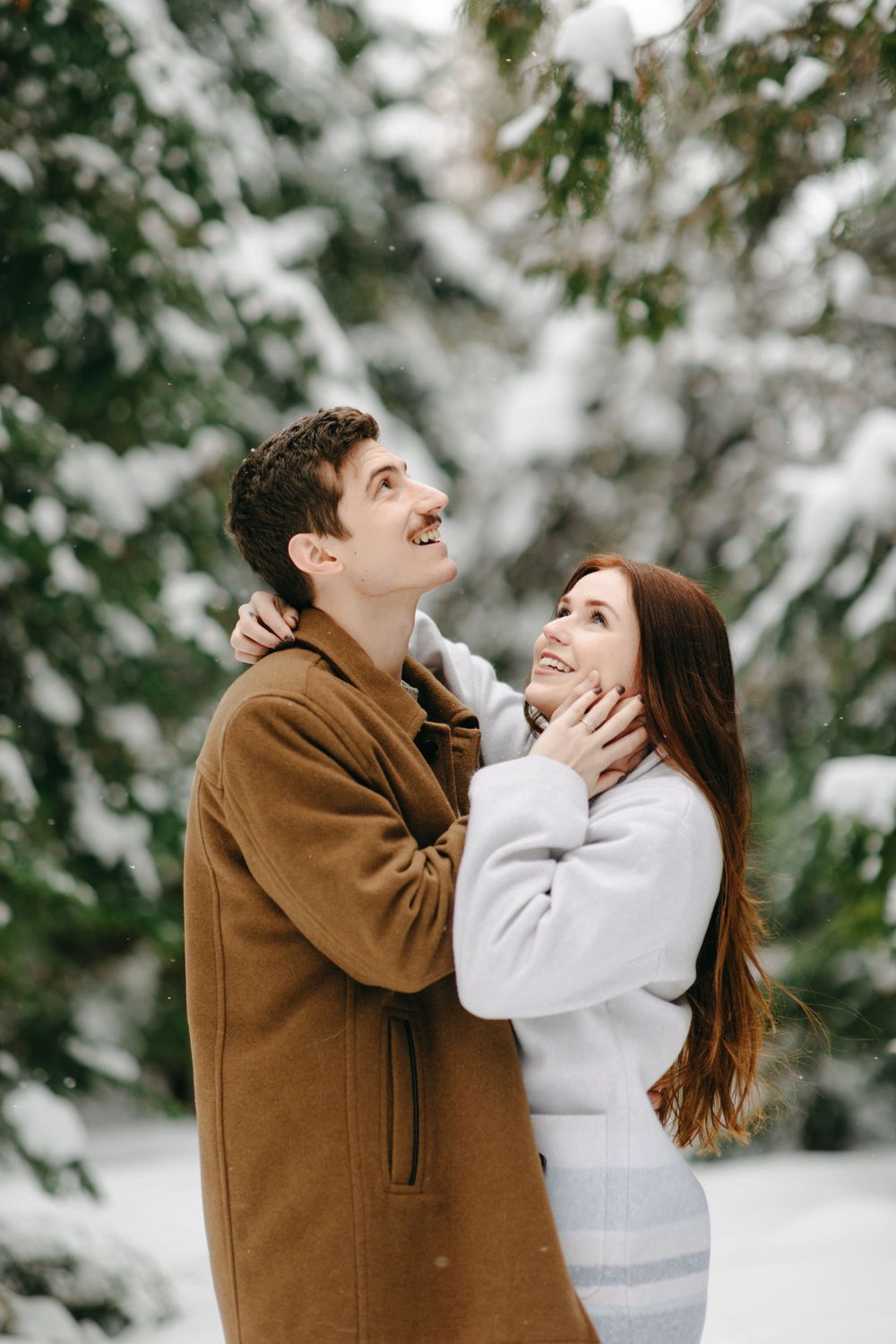 A couple shares a joyful moment together in a snowy winter forest setting.