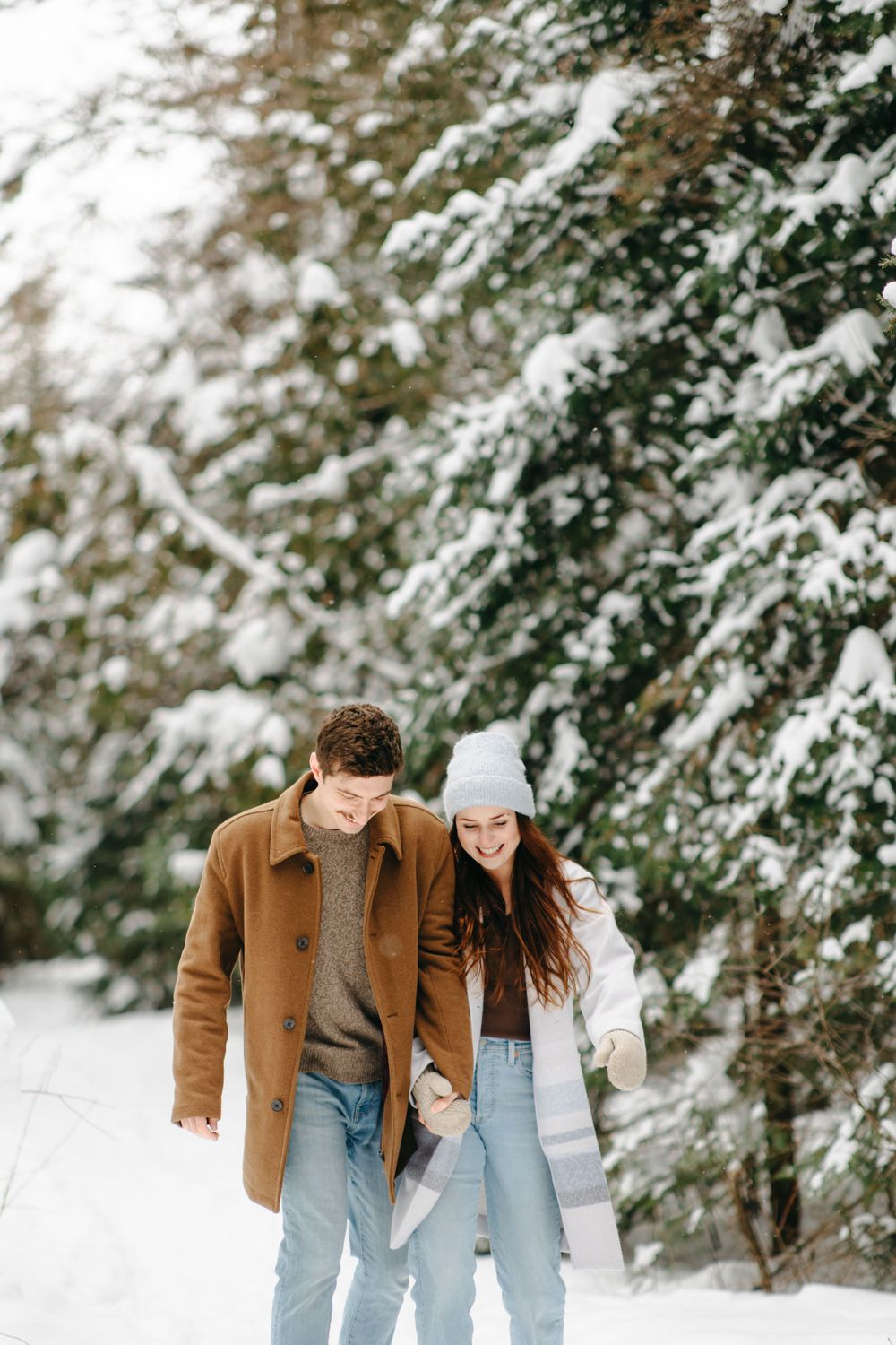 Couple walking together in a snowy winter forest wearing cozy coats and casual winter attire.
