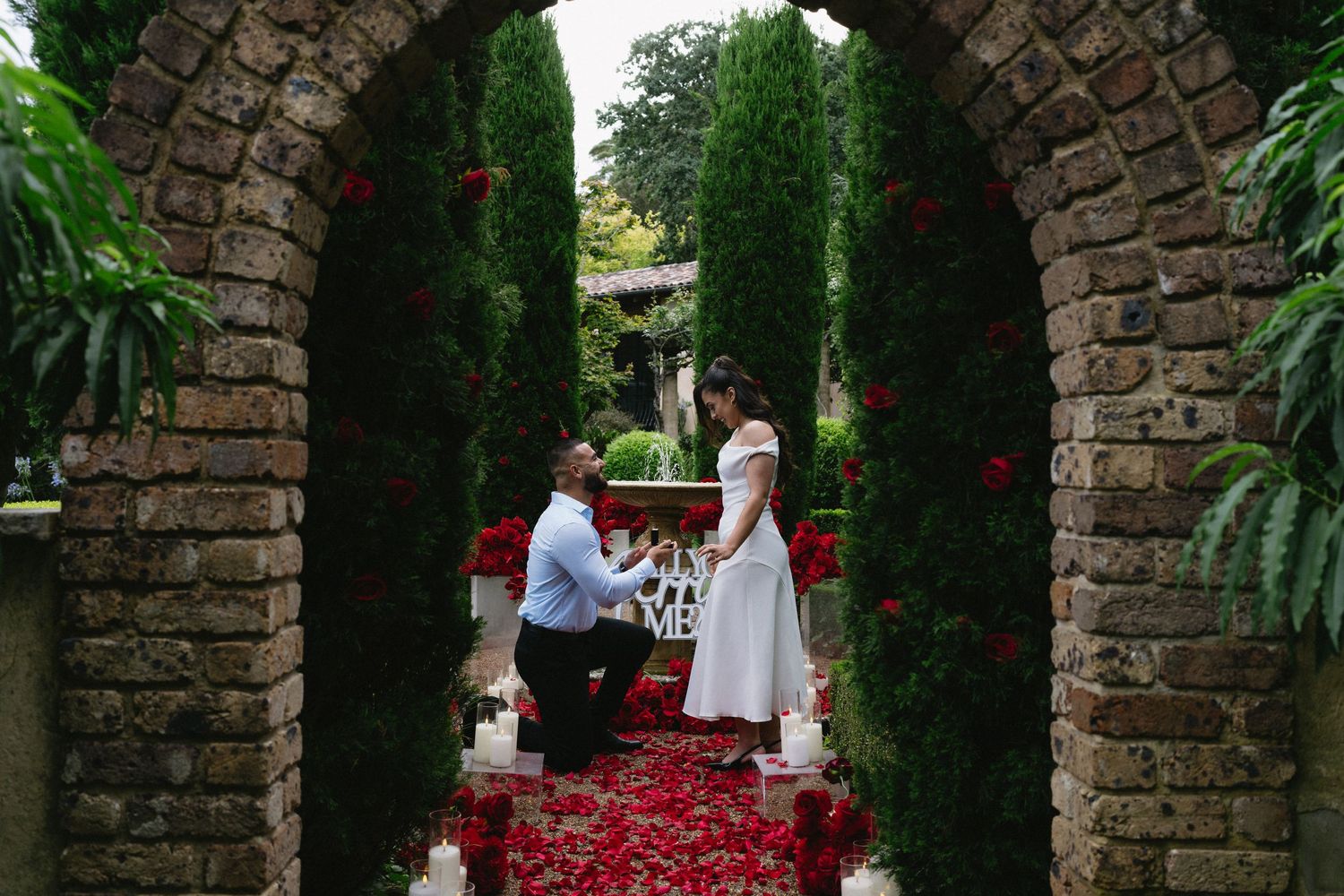 Marriage proposal through stone archway decorated with red rose petals.