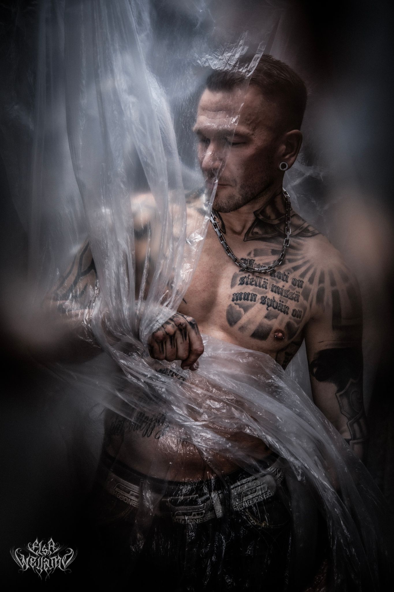 Artistic portrait of a shirtless man with tattoos surrounded by swirling smoke and plastic wrap effects.